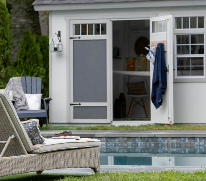 Pool shed with one door open. Poolside chair in foreground.