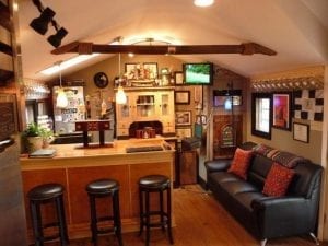 Man cave shed: Bar with three stools, couch, and wall art.