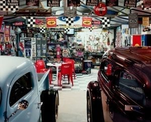Vintage Man Cave shed: Two cars, black and white checkered flooring and flags, white table surrounded by four red chairs.