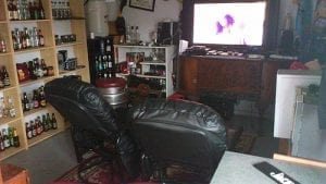 Man Cave shed: Two reclining chairs facing a TV. Wall of shelves with liquor bottles.