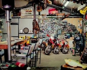 Man Cave shed: Long table with three tall chairs, three motorcycles, back wall full of photos.